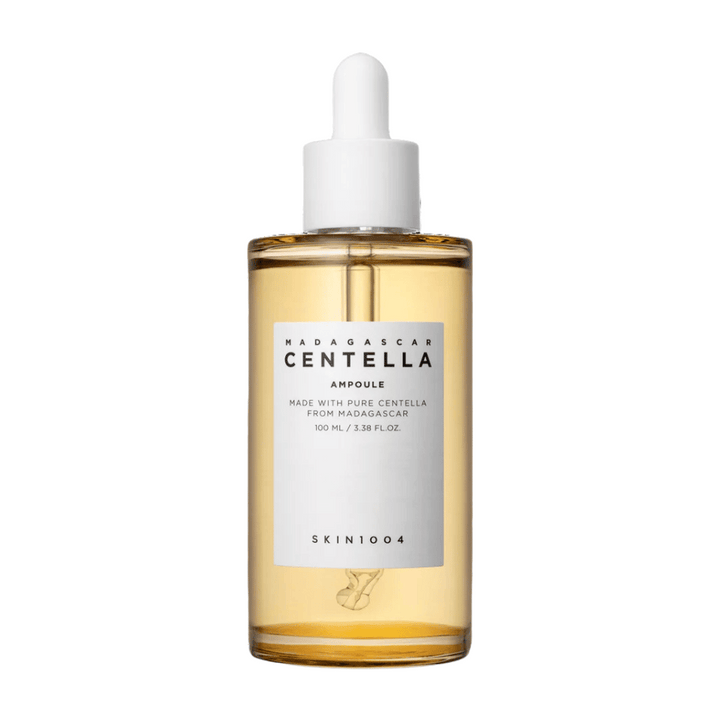 Bilden visar en flaska med "Madagascar Centella Asiatica 100 Ampoule" från SKIN1004. Flaskan innehåller 100 ml och påstår att vara gjord med ren Centella från Madagaskar. Produkten ser ut att vara en hudvårdsserum och den enkla etiketten ger ett intryck av renhet och naturlighet. Flaskan med droppkork föreslår att detta är en noggrant doserad hudvårdsprodukt.