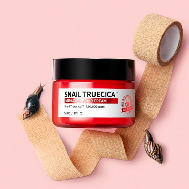 SOME BY MI's Snail Truecica Miracle Repair Cream 60g på rosa bakgrund, infunderad med teträd för klar hud.